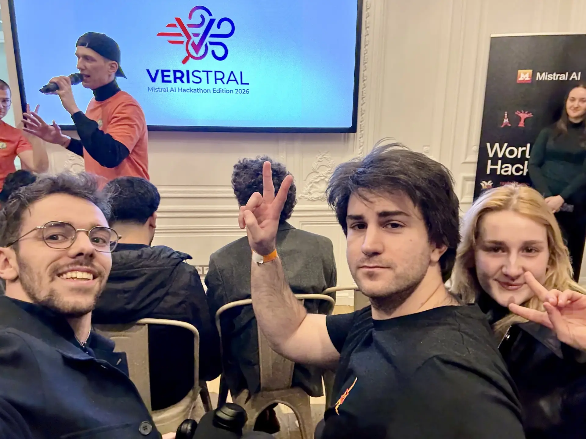 The team in front of the main screen showing the logo of our project. From left to right: Estéban, Godefroy, and Emma.